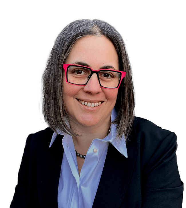 Smiling woman with shoulder-length gray hair wearing bright pink glasses, a light blue shirt, beaded necklace, and black blazer facing the camera.